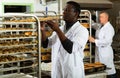 African baker arranging trays with bakery products on trolley Royalty Free Stock Photo