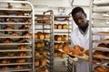 African baker placing tray with baked rolls on trolley