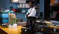 African barista standing with crossed arms behind a counter in a coffee shop and looking at a camera Royalty Free Stock Photo