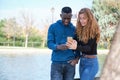 African black man and redhead caucasian woman smiling and looking at their smartphone in a park Royalty Free Stock Photo