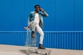 African black man sitting on a shopping cart talking on the phone, making a phone call Royalty Free Stock Photo