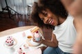 African blogger presenting cupcake with selfie on smartphone. Tastemaker.