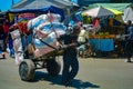 African boy carries a heavy handcart with bags of produce. Hard work in a marketplace, sunny day in Madagascar