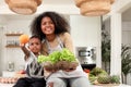 African boy child and mother with curly hair holding orange and healthy vegetable salad basket at kitchen, mom and son preparing Royalty Free Stock Photo