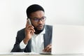 African businessman talking on phone and using laptop in office Royalty Free Stock Photo