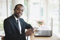 African businessman using mobile phone near laptop and coffee cup during a work break outdoors in cafe with smile and happy Royalty Free Stock Photo