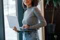 African businesswoman holding laptop and looking at camera while standing near window in coworking Royalty Free Stock Photo