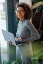 African businesswoman holding laptop and looking at camera while standing near window in coworking Royalty Free Stock Photo