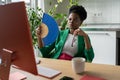 African businesswoman uses hand fan sits at desk with computer in summer day, suffers from heat. Royalty Free Stock Photo
