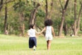 African and Caucasian little cute girls holding hands, walking together at green park, wear white vest. Diversity children friends Royalty Free Stock Photo