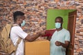 African client wearing a medical mask receiving a parcel from a young African courier