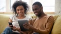 African couple resting on couch having fun using electronic gadgets Royalty Free Stock Photo