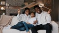 African couple sitting on couch under cardboard roof smiling looking at camera active happy daughter girl running sits Royalty Free Stock Photo