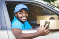 African courier of delivery company using smartphone and holding a box package in the car with smile and happy.Concept of business