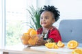 African cute kid girl try to lift fresh oranges basket up at home. Adorable child eating sliced orange with messy mouth. Healthy