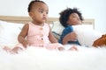 African cute toddle baby infant girl sitting white her relaxing brother boy lying down on white bed in bedroom. Portrait of Royalty Free Stock Photo