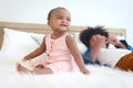 African cute toddle baby infant girl sitting white her relaxing brother boy lying down on white bed in bedroom. Portrait of Royalty Free Stock Photo