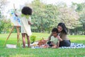 African daughter standing painting watercolor on canvas, Asian mother and little son sitting on grass playing wooden blocks toy, Royalty Free Stock Photo