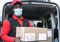 African delivery man carrying cardboard box while wearing face mask to avoid corona virus spread Royalty Free Stock Photo