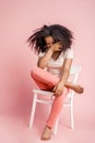 Freestyle. African girl sitting on chair isolated on pink covering face laughing happy Royalty Free Stock Photo