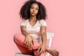 Freestyle. African girl sitting on chair isolated on pink relaxed close-up Royalty Free Stock Photo