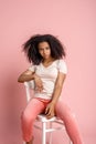 Freestyle. African girl sitting on chair isolated on pink posing cute Royalty Free Stock Photo