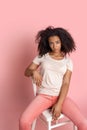 Freestyle. African girl sitting on chair isolated on pink posing smiling cute Royalty Free Stock Photo