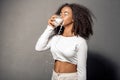 Freestyle. African girl in white outfit with bare belly standing isolated on gray drinking milk closed eyes joyful Royalty Free Stock Photo