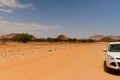 African desert dirt road with partial white car in hot red kalahari sand landscape with small trees and blue sky. Road Royalty Free Stock Photo