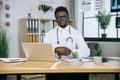 African doctor sitting at office desk with modern laptop Royalty Free Stock Photo