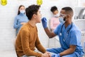 African Doctor Testing Asian Patient For Coronavirus Sitting In Clinic