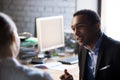 African employee talking with female colleague sitting together at workplace Royalty Free Stock Photo