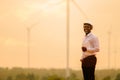 African engineer windmills wearing white hard hat and using tablet with   wind turbine on silhouette sunset Royalty Free Stock Photo