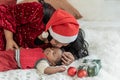 Nigerian mother wearing a red Christmas hat and kissing head her 4-month-old baby newborn son lying and sleeping in bed with happy Royalty Free Stock Photo