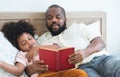 African family, single father and cute boy, lying on bed, reading a book together at home. Beard dad spends time and storytelling Royalty Free Stock Photo