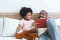 African family, single father and cute boy, lying on bed, reading a book together at home. Smiling beard dad spends time and have Royalty Free Stock Photo