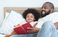 African family, single father and cute boy, lying on bed, reading a book together at home. Smiling beard dad spends time and have Royalty Free Stock Photo