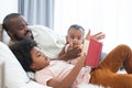 African family, single father, cute newborn baby and boy, lying on bed, reading a book together at home. Beard dad spends time, Royalty Free Stock Photo