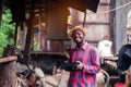 African farmer man with retro radio broadcast receiver on shoulder stands happy smiling outdoor on old cow stall background