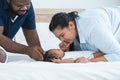 African father and Asian mother kissing hand of cute newborn baby sleeping lying on bed, smiling looking at innocent infant with Royalty Free Stock Photo