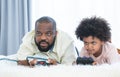 African father and child son playing online video games, using joysticks or game console, having fun at home while lying on bed Royalty Free Stock Photo