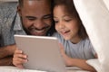 African father and daughter using tablet on bed under blanket Royalty Free Stock Photo