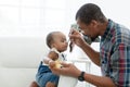 African father feeding adorable toddler baby girl with spoon while sitting on sofa at home and kid`s face mess up with food.