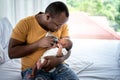 African father Sitting on bed, and feed milk from bottle milk to his 12-day-old baby black skin newborn Royalty Free Stock Photo