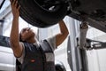 African female auto mechanic changing wheel tire in car in garage, side view Royalty Free Stock Photo