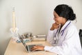 African female Doctor typing on laptop computer while sitting at the desk in hospital office. Physician at work. Royalty Free Stock Photo