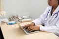 African female Doctor typing on laptop computer while sitting at the desk in hospital office. Physician at work. Royalty Free Stock Photo