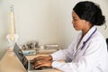 African female Doctor typing on laptop computer while sitting at the desk in hospital office. Physician at work. Royalty Free Stock Photo