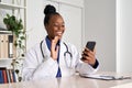 African female doctor video calling patient in online mobile phone app.