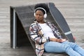 African female listen music outdoors wear casual clothes with skateboard sit on bench in urban space